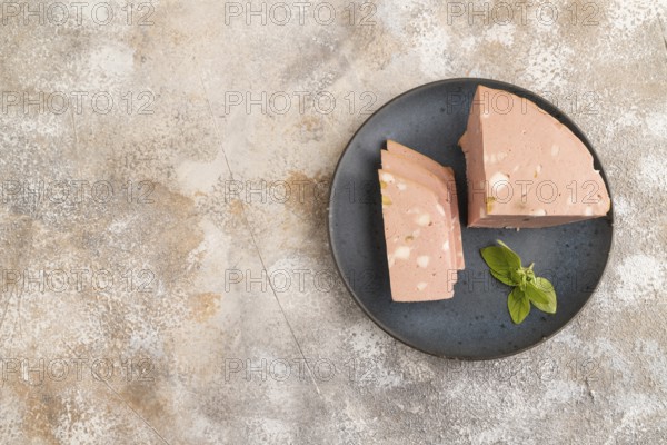 Mortadella sausage on plate with pepper and herbs on brown concrete background. Top view, flat lay,