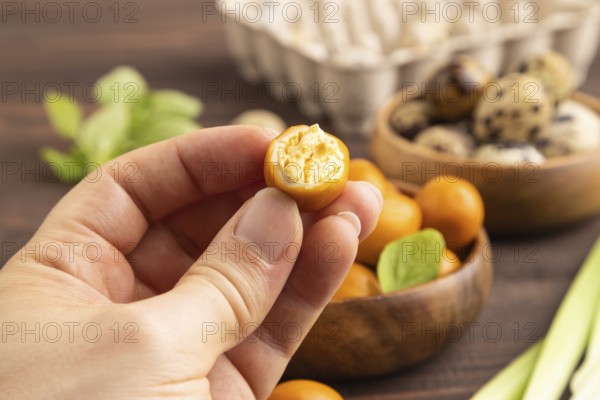 Pile of Smoked Quail eggs in bowl with hand on a brown wooden background. side view, close up,