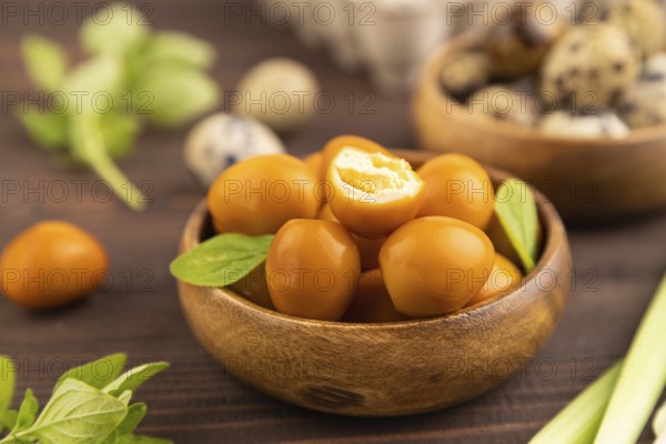 Pile of Smoked Quail eggs in bowl on a brown wooden background. side view, close up, selective