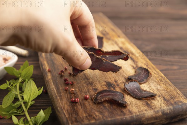 Armenian Basturma dried meat with hand on wooden cutting board with pepper and herbs on brown
