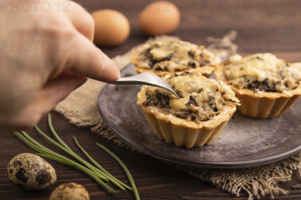 Tartlets with meat and cheese with hand on brown wooden background and linen textile. side view,