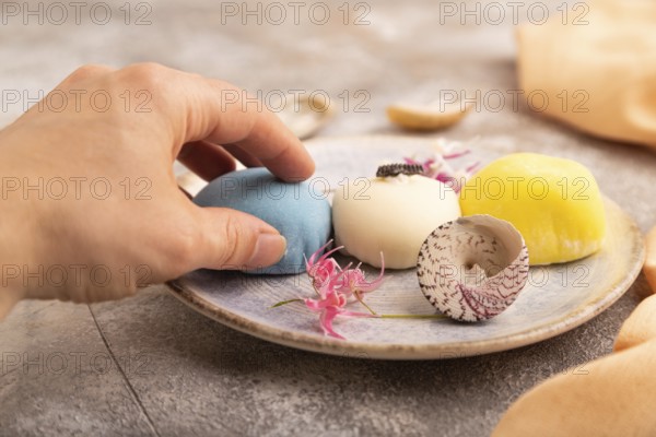 Japanese Mochi Cakes with hand on brown concrete background and orange textile, side view, close