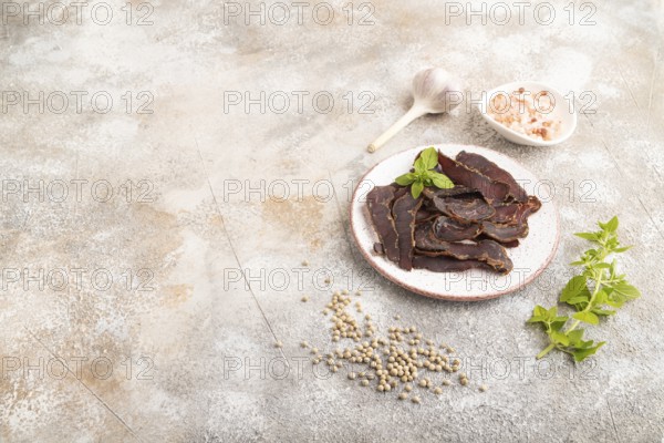 Armenian Basturma dried meat on plate with pepper and herbs on brown concrete background. Side