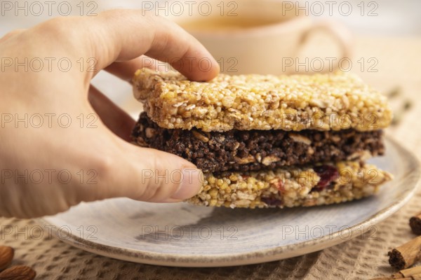 Granola bars with caramel, nuts, flakes in ceramic plate on brown concrete background with hand,