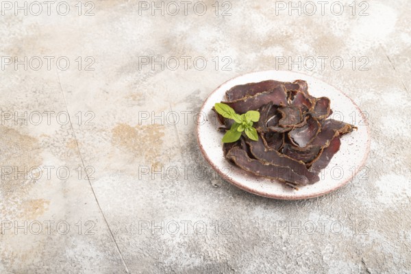 Armenian Basturma dried meat on plate with pepper and herbs on brown concrete background. Side