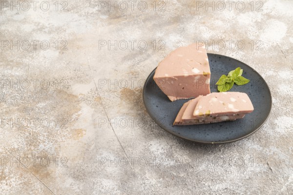 Mortadella sausage on wooden cutting board with pepper and herbs on brown concrete background. Side