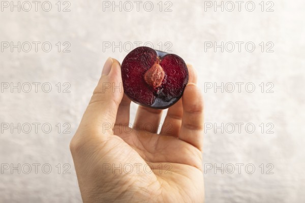 Purple Plum Cut in half with hand on gray concrete background. Side view, close up. healthy food,