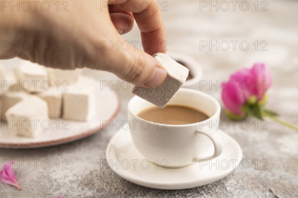 Coffee marshmallow with cup of coffee with hand on brown concrete background. side view, close up,