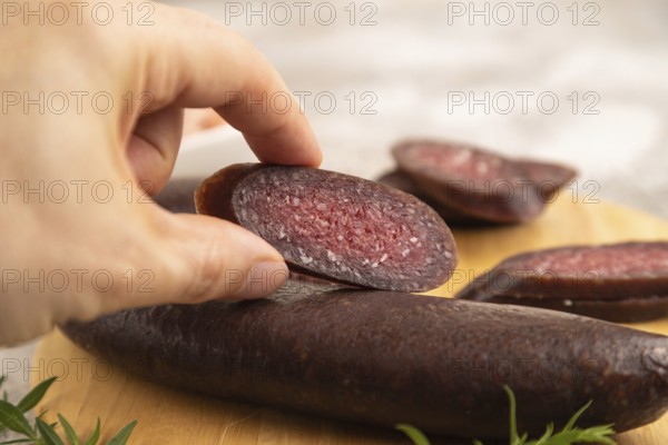 Sujuk sausage with hand on wooden cutting board with pepper and herbs on brown concrete background.