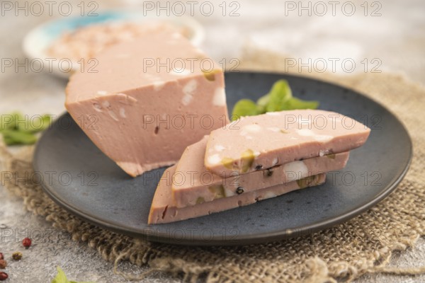 Mortadella sausage on plate with pepper and herbs on brown concrete background and linen textile.