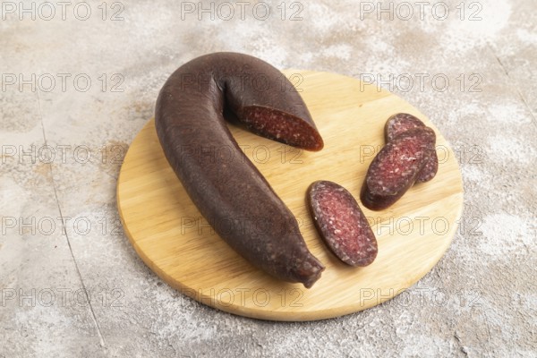 Sujuk sausage on wooden cutting board with pepper and herbs on brown concrete background. Side