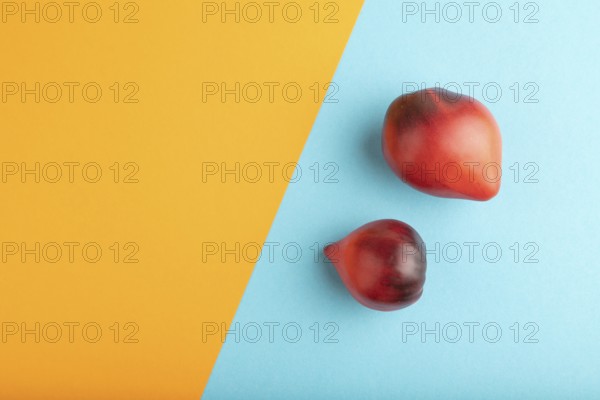 Red Heart shape tomatoes on blue and orange pastel paper background. Top view, copy space, flat lay