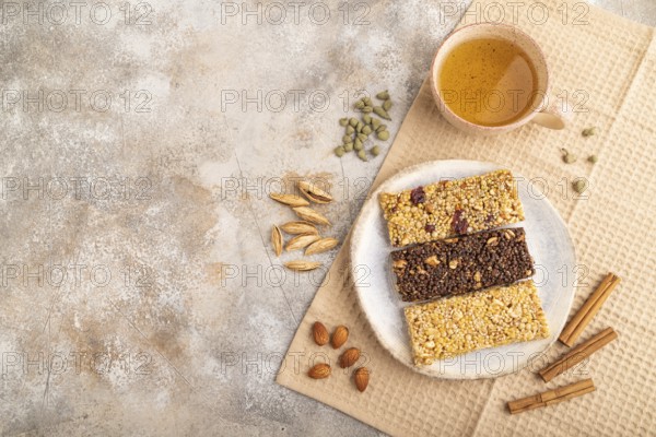 Granola bars with caramel, nuts, flakes in ceramic plate on brown concrete background, beige linen