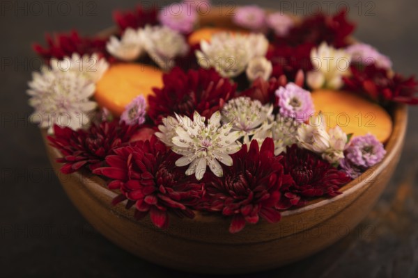 Wooden bowl with carrot slices and red Chrysanthemum flowers, Astrantia flowers, flower salad on