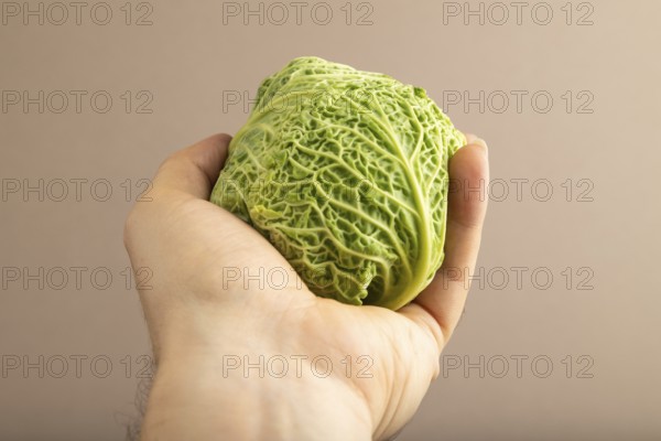 Green lettuce with hand on beige pastel paper background. Side view, copy space, flat lay. healthy