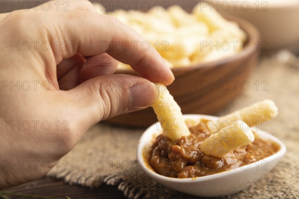 Corn flakes sticks with caramel in wooden bowl with hand on brown wooden background and linen