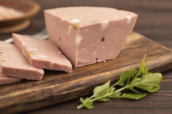Mortadella sausage on wooden cutting board with pepper and herbs on brown wooden background. Side