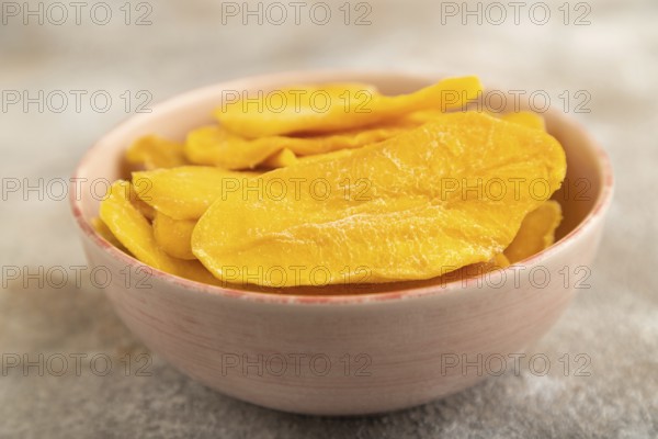 Dried Mango in ceramic bowl on brown concrete background. Side view, close up, selective focus.