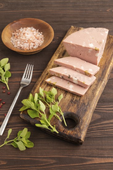 Mortadella sausage on wooden cutting board with pepper and herbs on brown wooden background. Side
