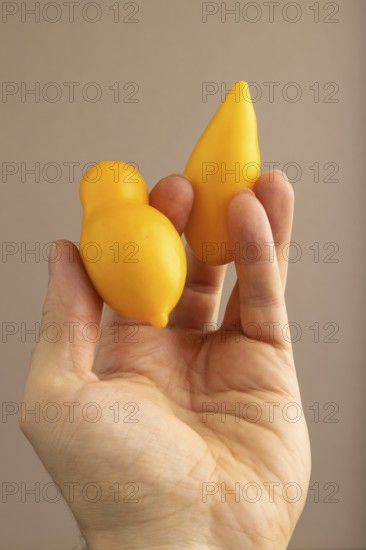 Yellow tomatoes with hand on beige pastel paper background. Side view, copy space. healthy food,
