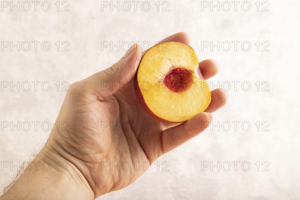 Peach Cut in half with hand on brown concrete background. Side view, copy space. healthy food,