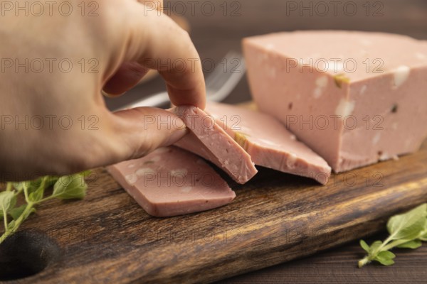 Mortadella sausage with hand on wooden cutting board with pepper and herbs on brown wooden