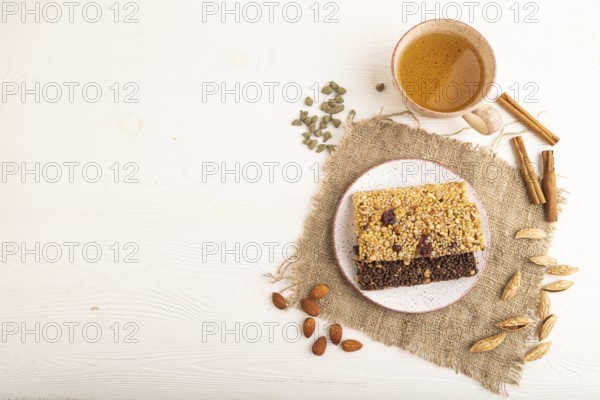 Granola bars with caramel, nuts, flakes in ceramic plate on white wooden background, beige linen