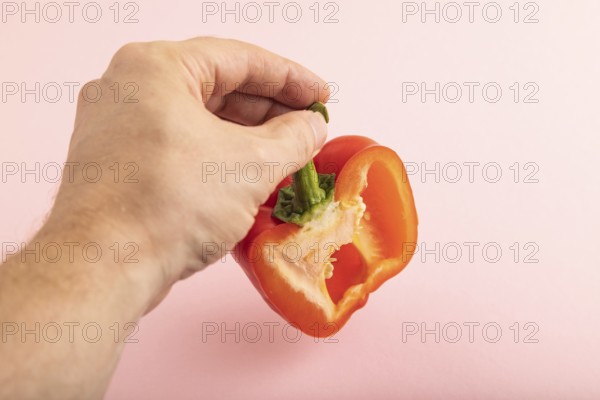 Hand holding sliced Red Cutted pepper on pink pastel background. Side view, copy space. Tropical,