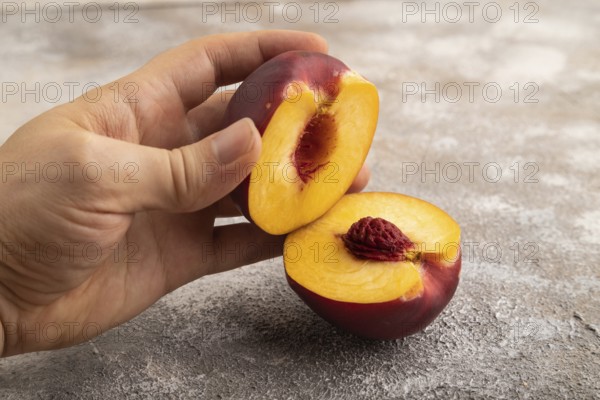 Peach Cut in half with hand on brown concrete background. Side view, copy space. healthy food,