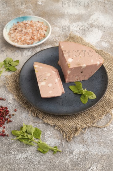 Mortadella sausage on plate with pepper and herbs on brown concrete background and linen textile.
