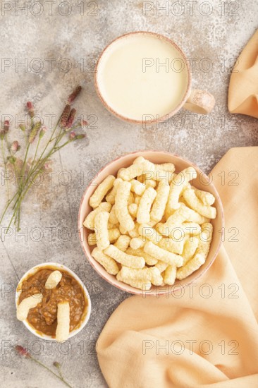 Corn flakes sticks with caramel in ceramic bowl on gray concrete background and orange linen