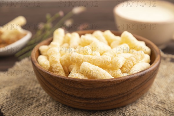 Corn flakes sticks with caramel in wooden bowl on brown wooden background and linen textile. Side