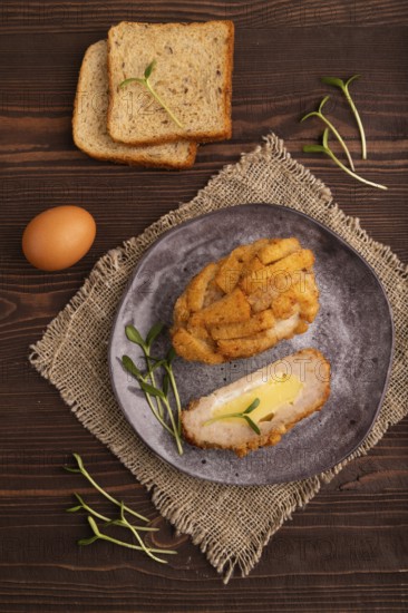 Chicken Schnitzel on gray plate with microgreen on brown wooden background and linen textile. top