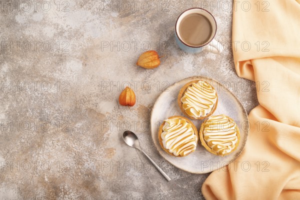French lemon tart with meringue on brown concrete background, cup of coffee, orange linen textile,