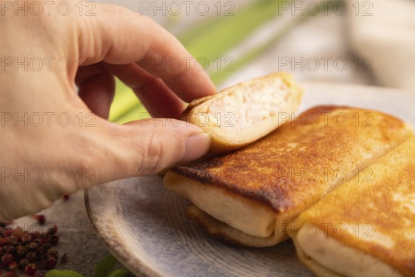 Fried crispy pancakes with meat and cheese with hand on brown concrete background and linen textile
