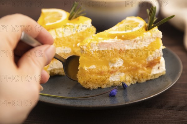 Lemon cake with hand on brown wooden background and linen textile, cup of coffee, side view, close