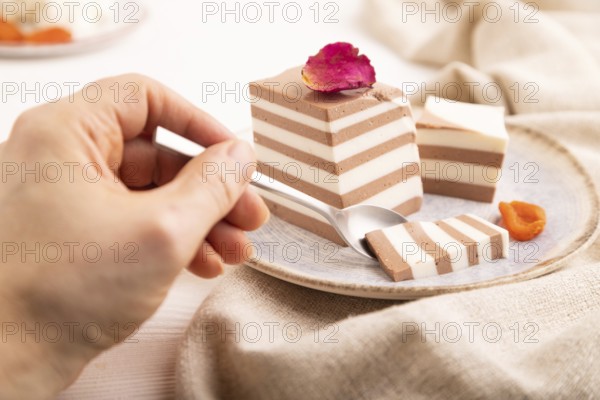 Cocoa and milk jelly with dried apricots with hand on white wooden background and linen textile,