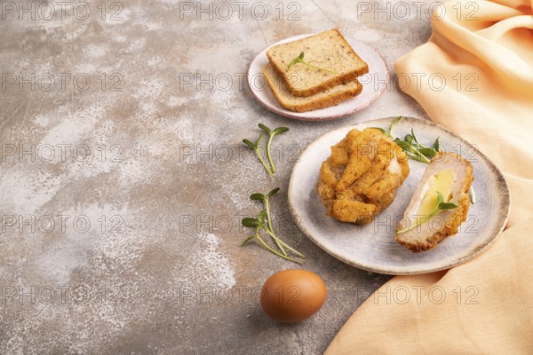 Chicken Schnitzel on blue plate with microgreen on brown concrete background and orange linen