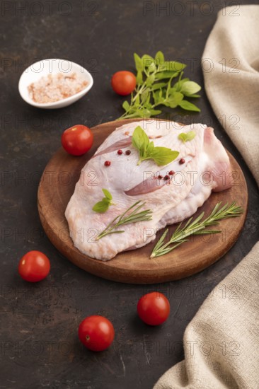 Raw Turkey Thigh with spices and rosemary on cutting board on black concrete background and linen