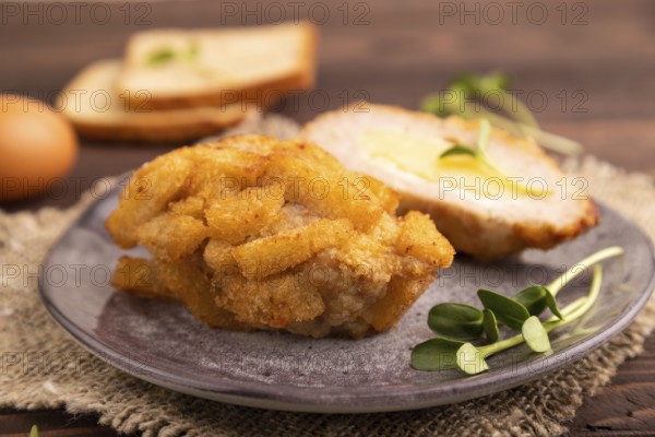 Chicken Schnitzel on gray plate with microgreen on brown wooden background and linen textile. side
