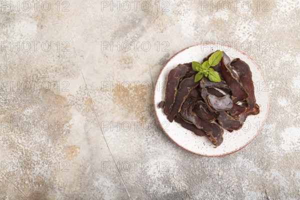 Armenian Basturma dried meat on plate with pepper and herbs on brown concrete background. Top view,