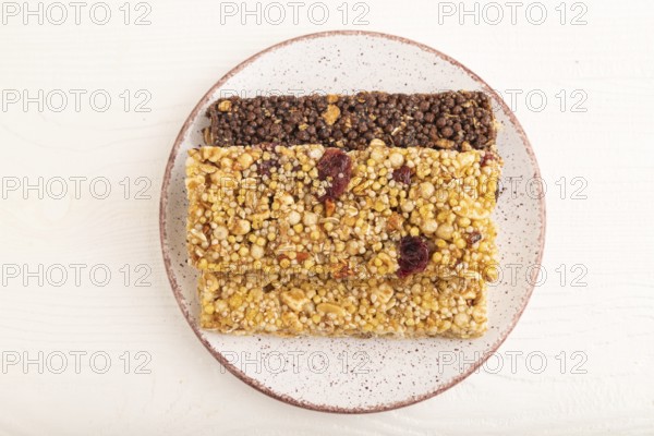 Granola bars with caramel, nuts, flakes in ceramic plate on white wooden background. Top view, flat