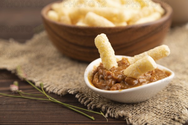 Corn flakes sticks with caramel in wooden bowl on brown wooden background and linen textile. Side