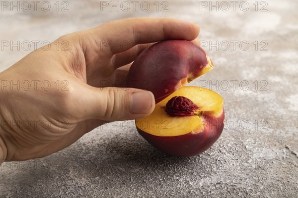 Peach Cut in half with hand on brown concrete background. Side view, copy space. healthy food,