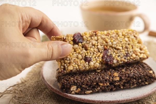 Granola bars with caramel, nuts, flakes in ceramic plate with hand on white wooden background,