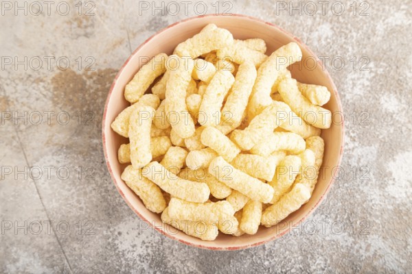Corn flakes sticks with caramel in ceramic bowl on gray concrete background. Top view, flat lay,