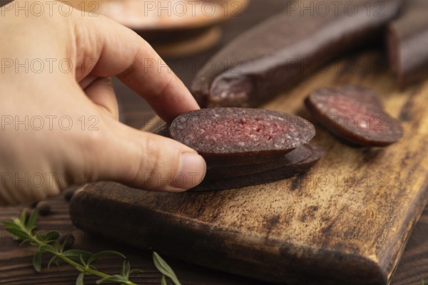 Sujuk sausage with hand on wooden cutting board with pepper and herbs on brown wooden background.