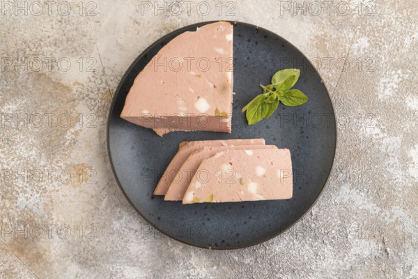 Mortadella sausage on plate with pepper and herbs on brown concrete background. Top view, flat lay,