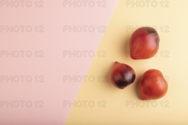 Red Heart shape tomatoes on pink and orange pastel paper background. Top view, copy space, flat lay