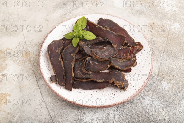 Armenian Basturma dried meat on plate with pepper and herbs on brown concrete background. Side